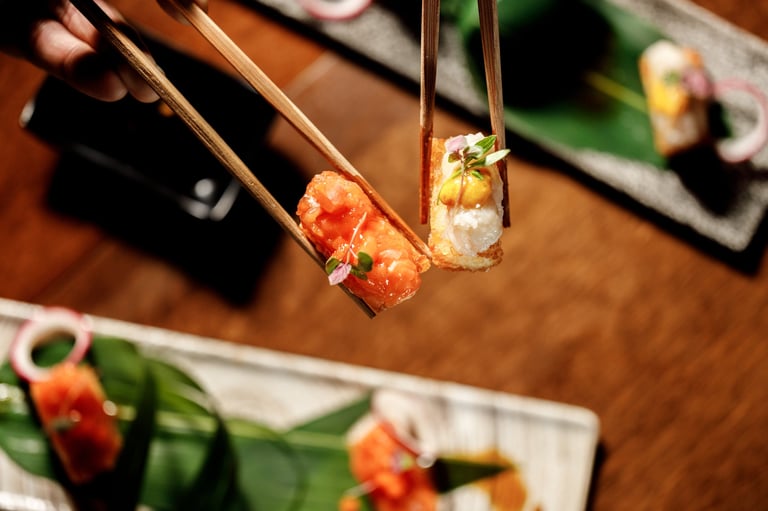 Chopsticks holding two shrimp appetizers with red sauce and garnish over wooden table