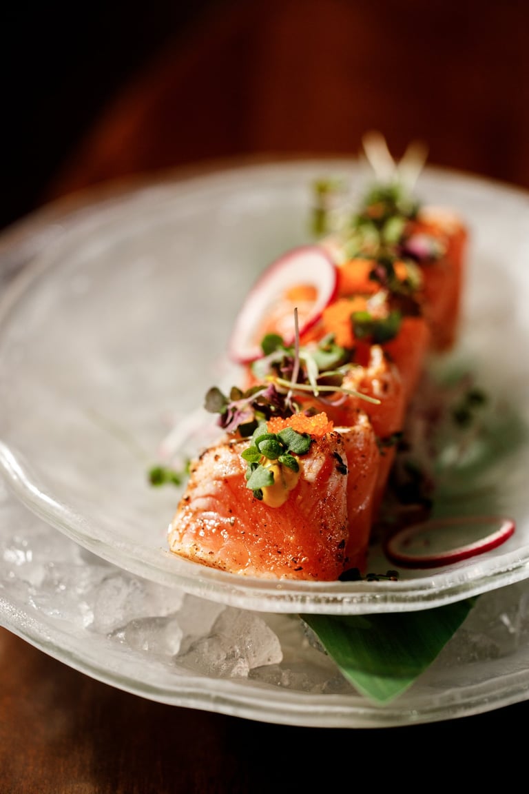 Elegant sashimi-style salmon pieces topped with microgreens and radish slices on a white plate