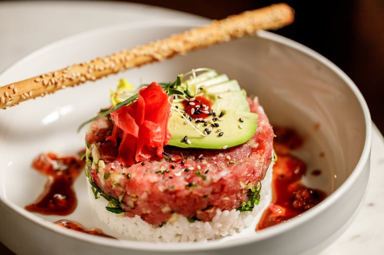 Plated tuna tartare topped with avocado and microgreens, garnished with crispy sesame stick